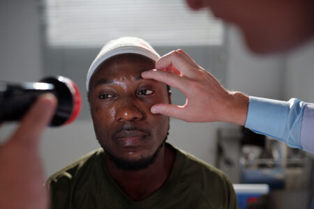 Doctor using flashlight to examine the eyesight of patient after injury in hospital