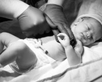 A greyscale closeup of a doctor checking a newborn child under the lights in a hospital