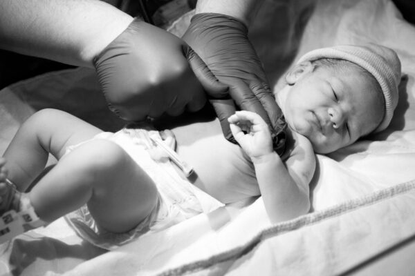 A greyscale closeup of a doctor checking a newborn child under the lights in a hospital